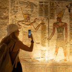 Woman using smartphone and taking picture while visiting the inner rooms inside the temple of Abu Simbel, in southern Egypt in Nubia next to Lake Nasser. Temple of Pharaoh Ramss II