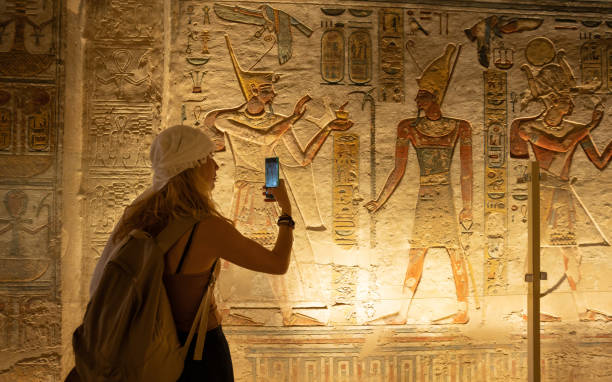 Woman using smartphone and taking picture while visiting the inner rooms inside the temple of Abu Simbel, in southern Egypt in Nubia next to Lake Nasser. Temple of Pharaoh Ramss II