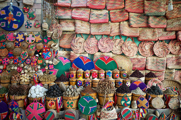 "Colorful woven baskets and bags fill the space around piles of spices and herbs in a market stall in the souk in Aswan, Egypt"