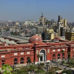 Cairo, Egypt -- March 15, 2003: Panoramic view of the Egyptian Museum to the west north side of town at noon. Palm trees are in the garden. At the background, neon lights are installed on the roofs of the buildings.